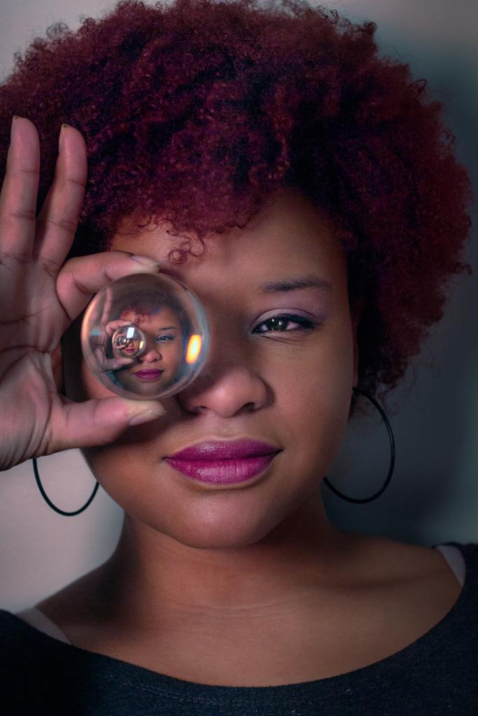Woman holding a clear glass ball over her right eye
