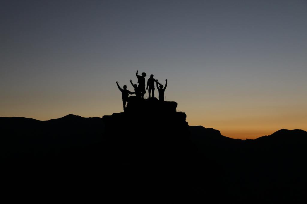 Silhouette of people standing on a rock at sunset, their hands in the air