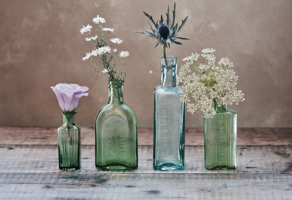 Four glass vases, three green and one blue, each holding a different flower