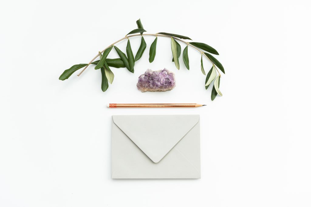 Green leaves, a purple crystal a pencil and an envelope aligned on a white background