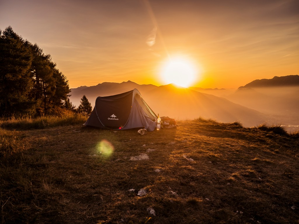 Dome tent in the mountains, with the sun just above the horizon