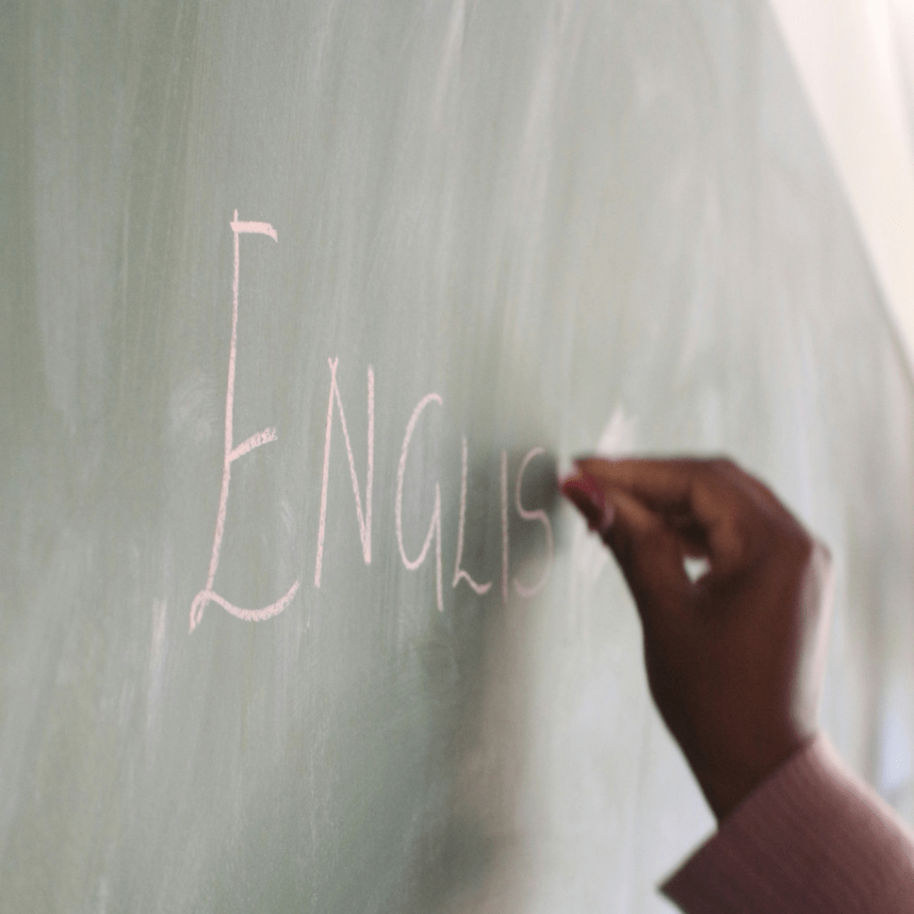 A hand writing the word 'ENGLISH' on a green chalkboard.