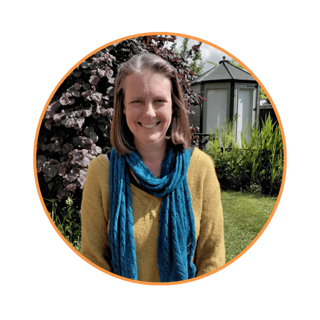 Woman wearing a yellow sweater and blue scarf in a garden (Jodie Clark). 
